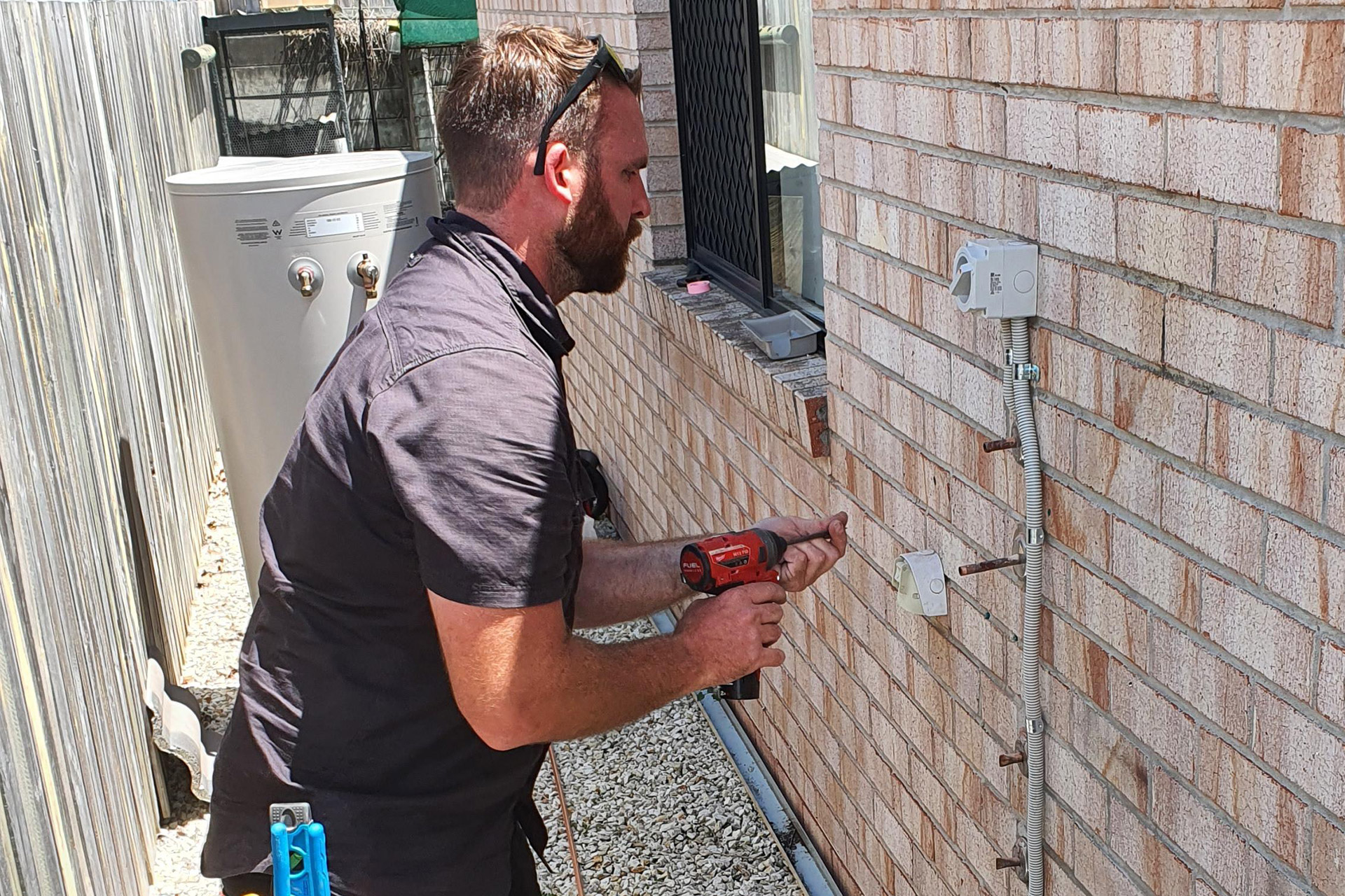 A licensed fitter installs a new hot water system at a home.