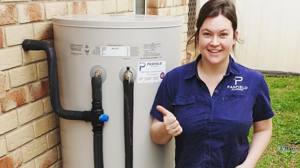 Pasfield Plumbing office manager Jess giving a thumbs up beside a new hot water system.